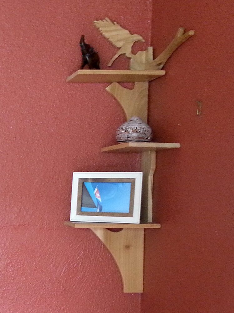 Handcrafted Poplar Bird and Tree Corner Shelf hanging in the corner on a red wall slanted to the left.