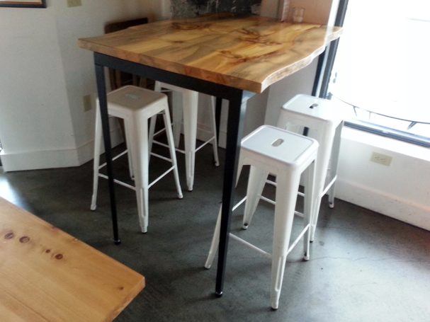 A commercial quality Blue Pine Live Edge Slab Table Top dining table slanted to the right at a restaurant bar.