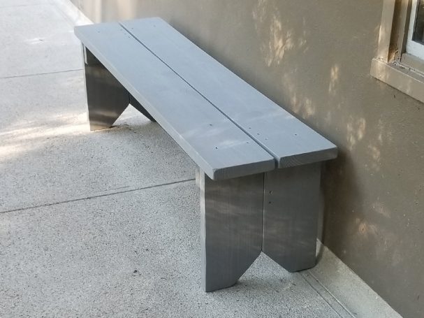 Gray Commercial quality eco-friendly Outdoor Farmhouse Bench slightly slanted to the left in front of a house.